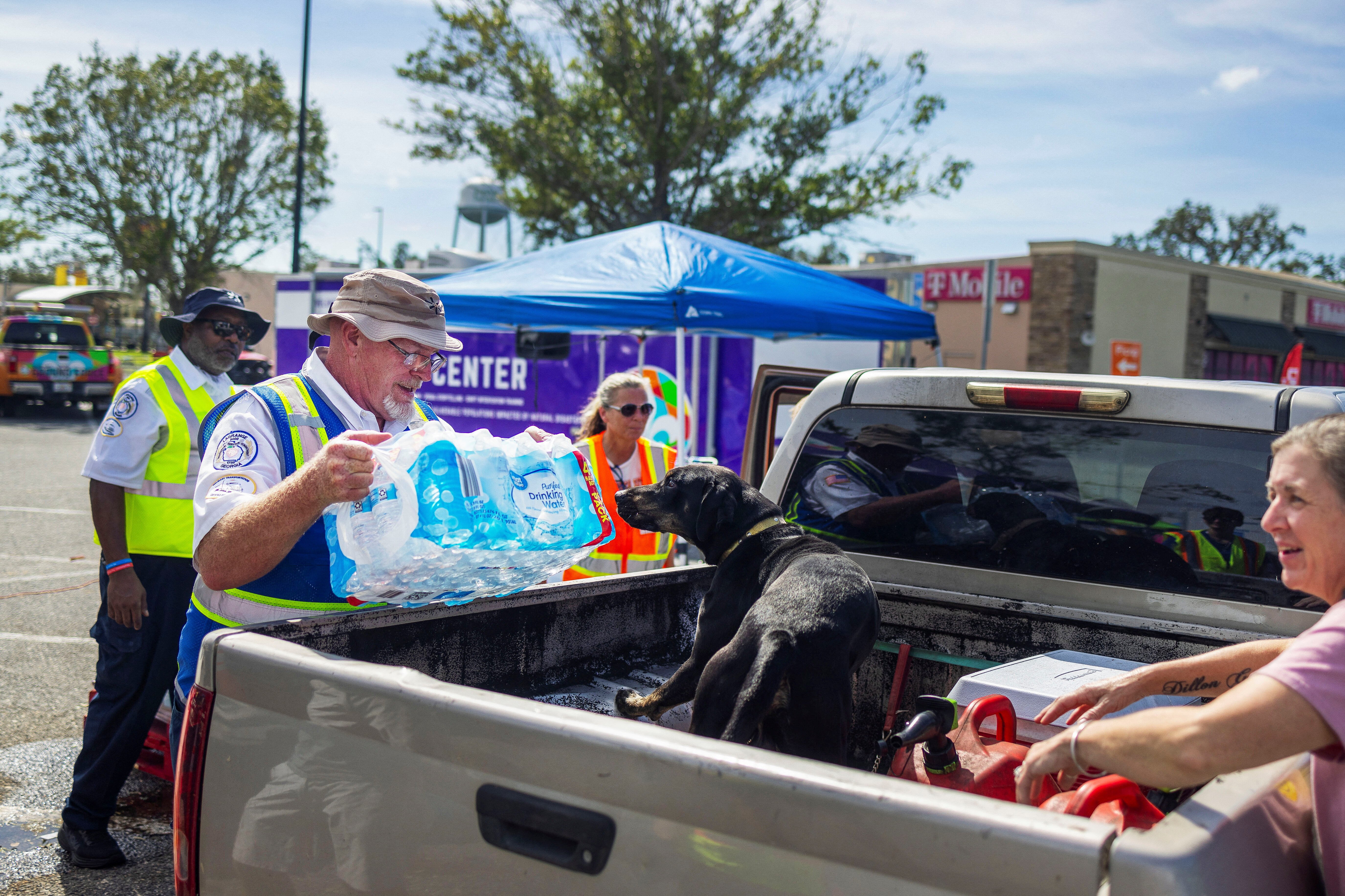 Michael Condon, of LaGrange in Georgia, places a case of water at the back of Angela Dixon's car as her dog Ammo watches during a Walmart Mobile Relief Kitchen and Ground Force Humanitarian Aid distribution in the wake of Hurricane Helene in Perry, Florida, U.S., September 28, 2024. REUTERS/Kathleen Flynn