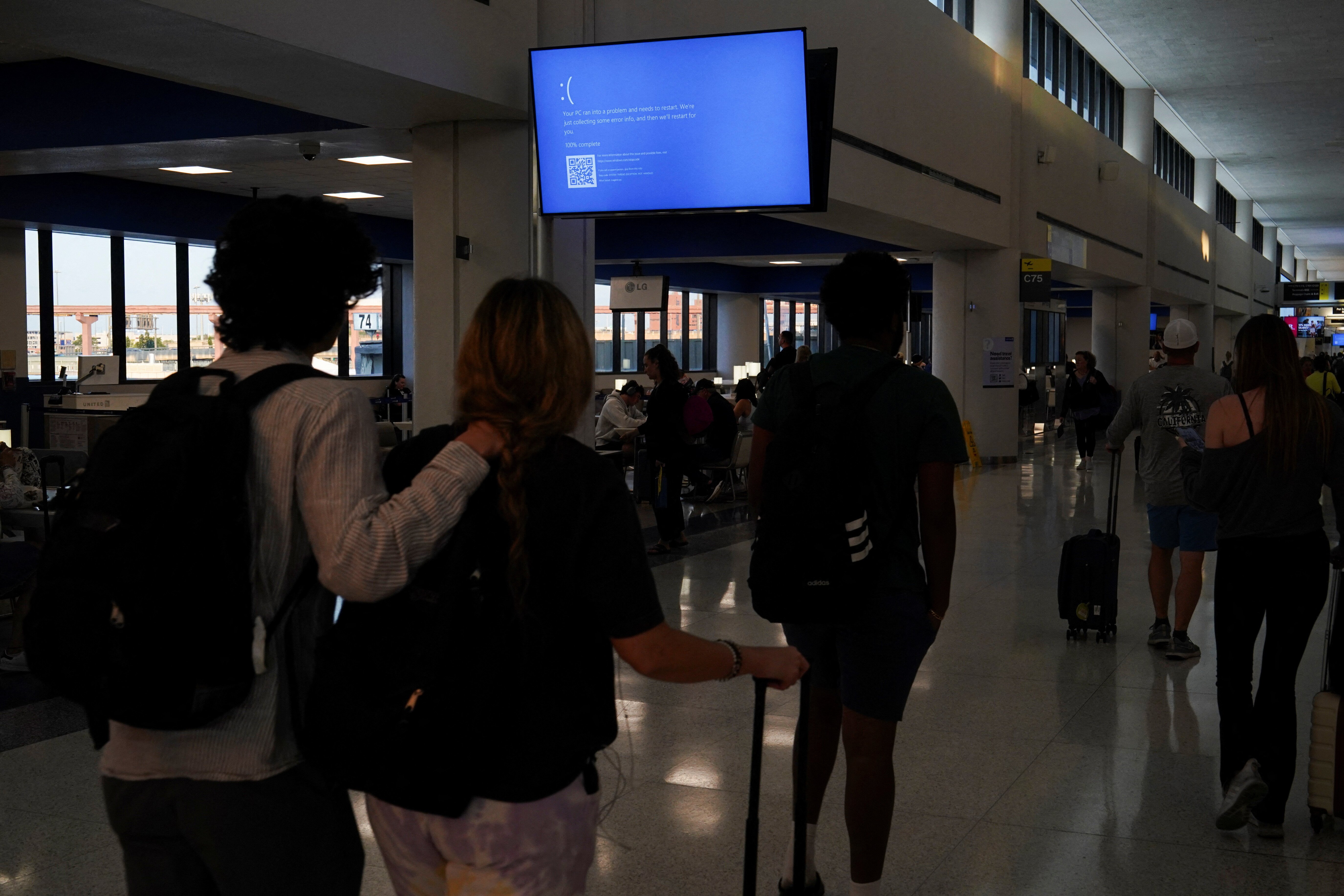 Travelers walk past a monitor displaying a blue error screen, also known as the “Blue Screen of Death” inside Terminal C in Newark International Airport, after United Airlines and other airlines grounded flights due to a worldwide tech outage caused by an update to Crowdstrike's 