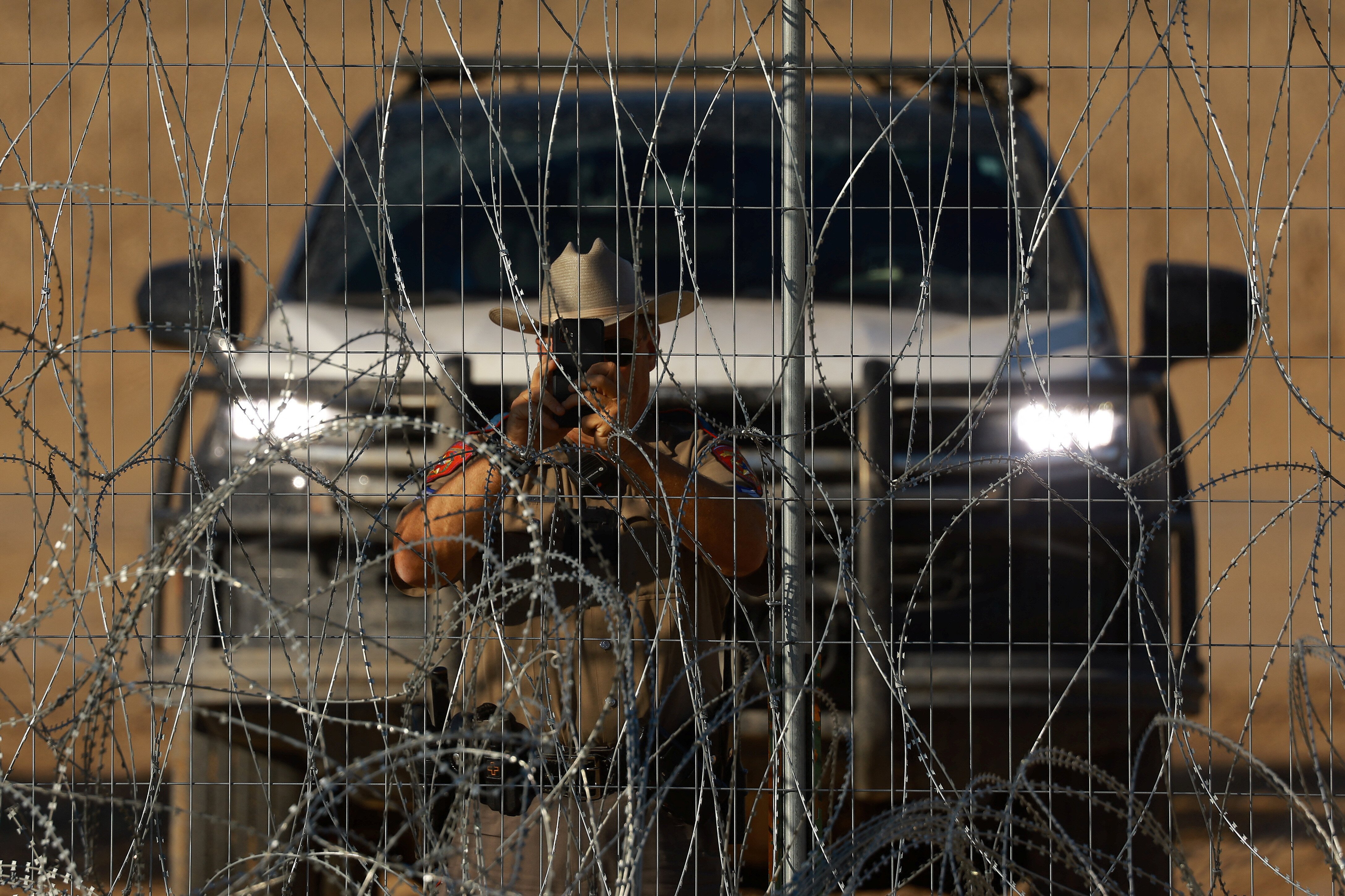 A Texas Department of Public Safety (DPS) trooper takes photographs with his cell phone near a razor wire fence, used to prevent migrants from crossing into the United States, at the U.S.-Mexico border, as seen from Ciudad Juarez, Mexico August 14, 2024. REUTERS/Jose Luis Gonzalez