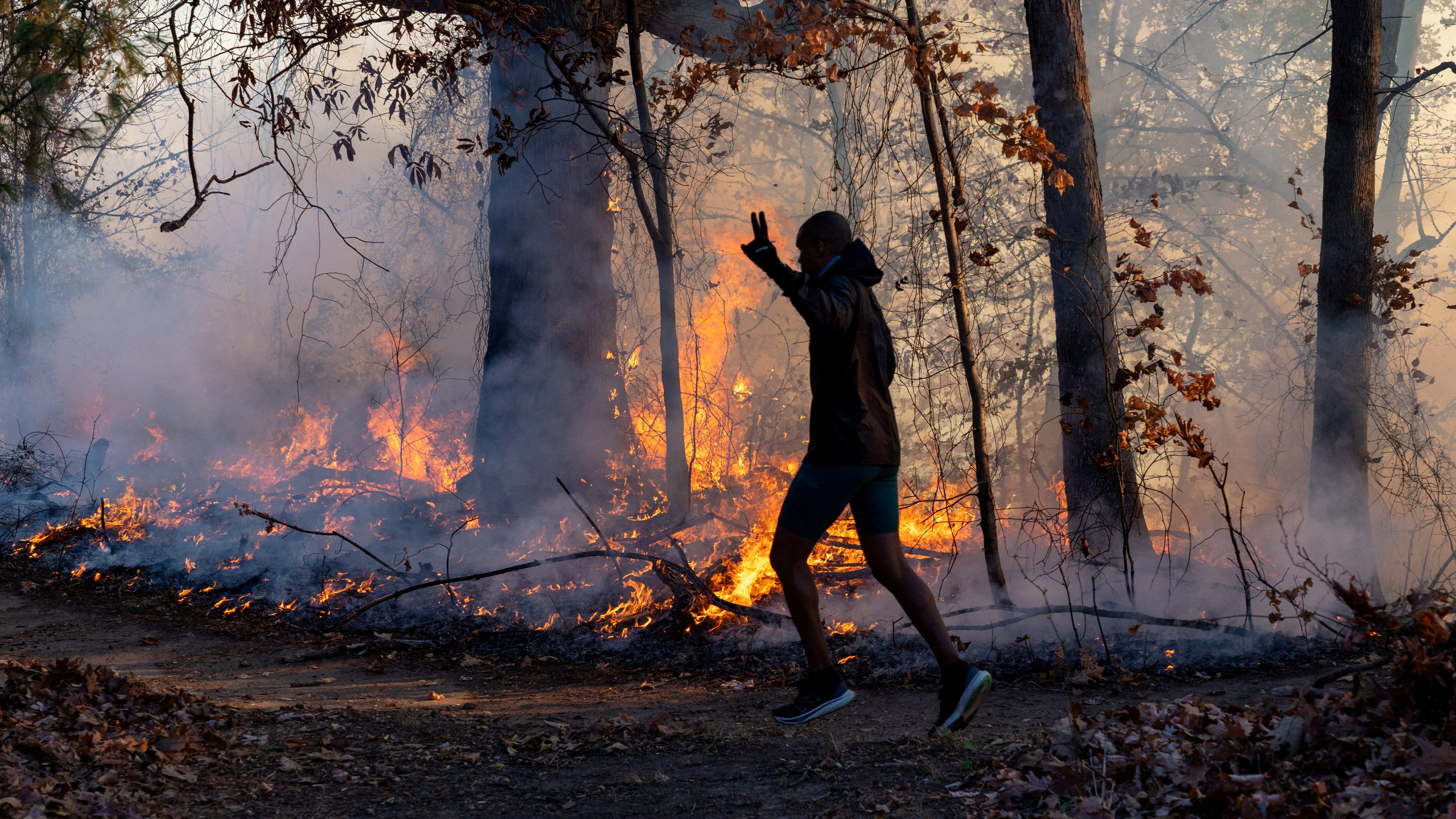 A morning jogger gestures as he runs past a fire lit by members of the New Jersey Forest Fire Service as part of back burning efforts alongside Palisades Interstate Parkway in Englewood Cliffs, New Jersey, U.S., November 8, 2024. Julian Leshay Guadalupe/NorthJersey.com / USA TODAY NETWORK via REUTERS