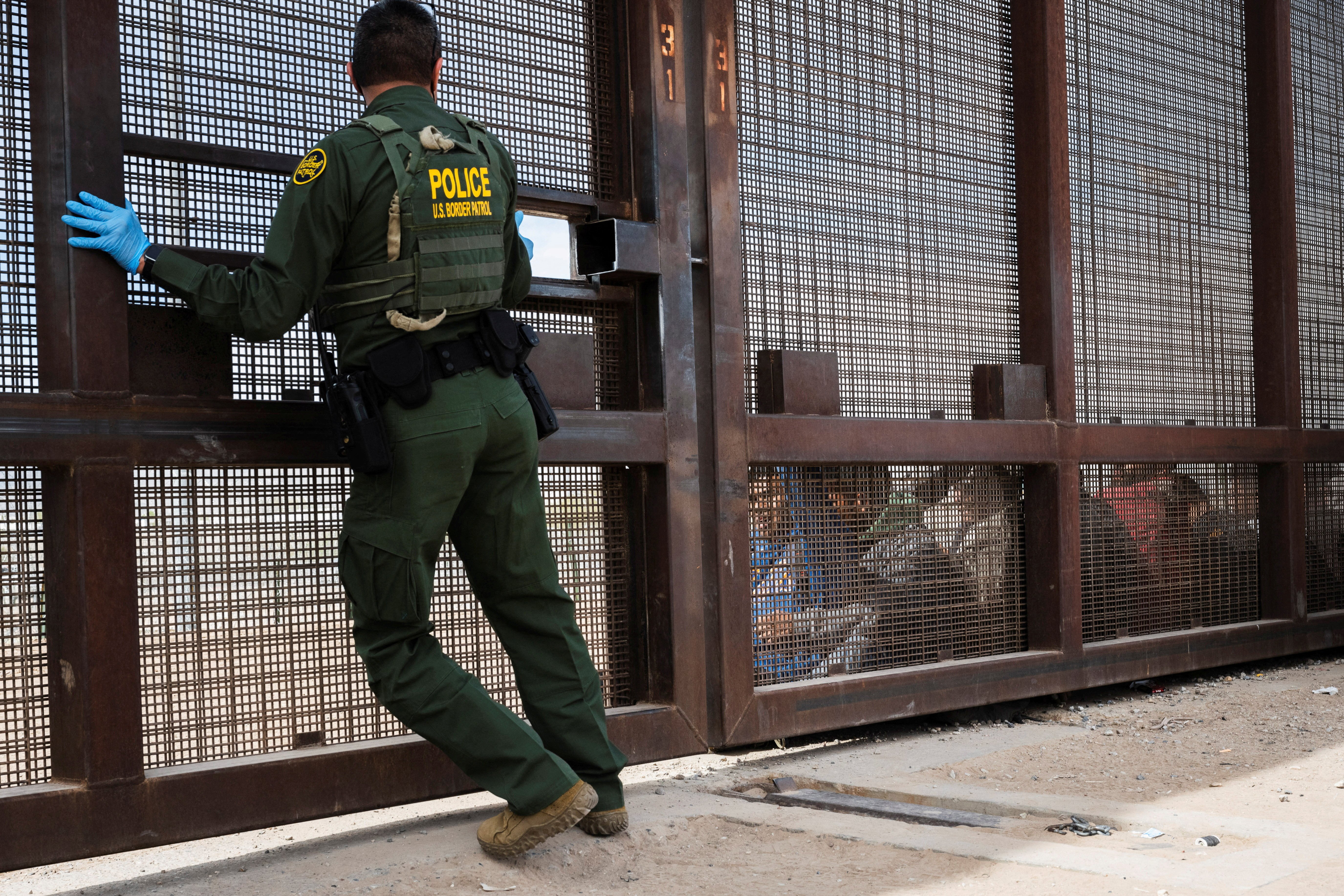 A Border Patrol agent opens a gate in the border wall to search a group of migrants that were let through concertina wire by Texas National Guard on the day the U.S. 5th Circuit Court of Appeals hears oral arguments on Texas' motion to lift a block on its SB4 immigration law that would allow state officials to arrest migrants suspected of being in the country illegally, in El Paso, Texas, U.S. March 20, 2024 . REUTERS/Justin Hamel