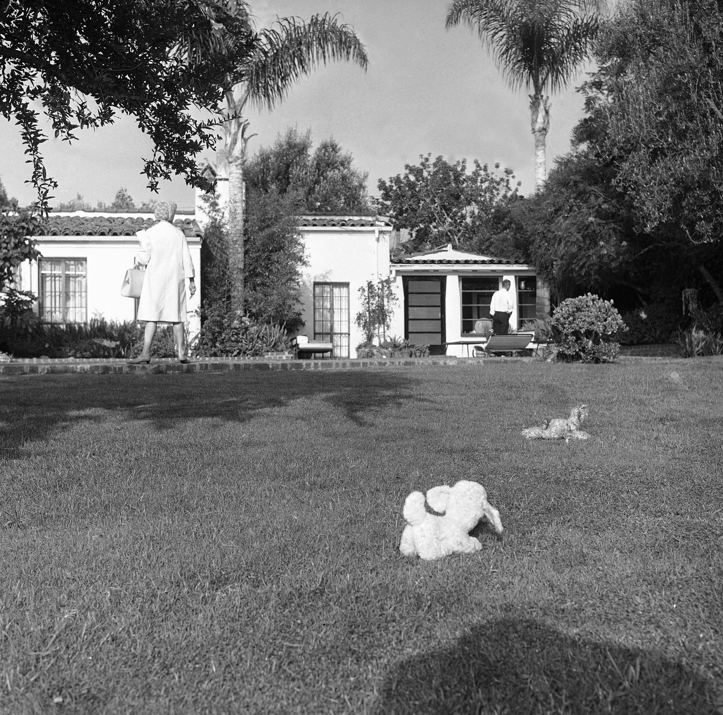 Toys for her dog - a lamb and a teddy bear -- lie on the backyard grass of the home of Marilyn Monroe after she was found dead in Hollywood, August 5, 1962. Police found them in this position when they arrived to find the star dead in her bed, a bottle of sleeping pills nearby. A newswoman stands at left. (AP Photo/Harold Filan)